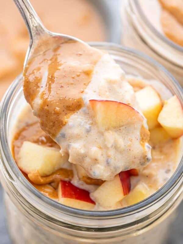 Spoon scooping up peanut butter overnight oats with chopped apples.