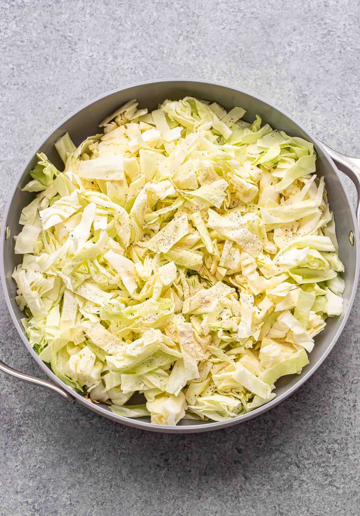 Thinly sliced cabbage in a skillet before it's been cooked.