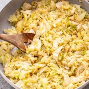 Skillet of sauteed cabbage with a wooden serving spoon in it.