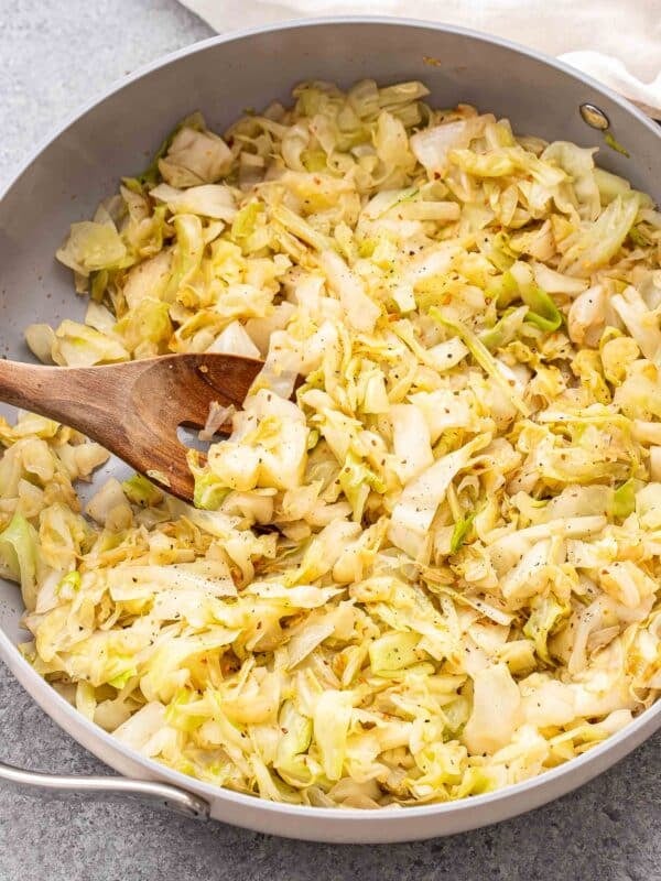 Skillet of sauteed cabbage with a wooden serving spoon in it.