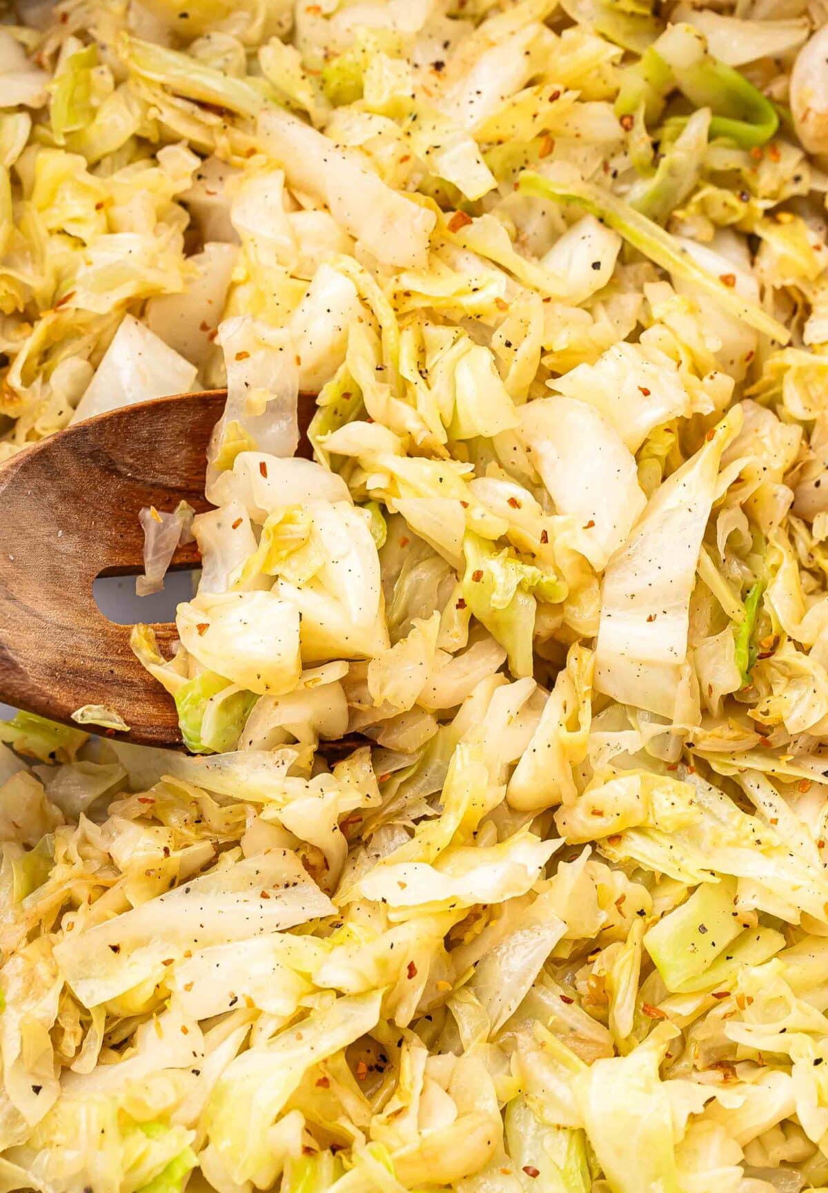 Sauteed cabbage with a wooden serving spoon in it.