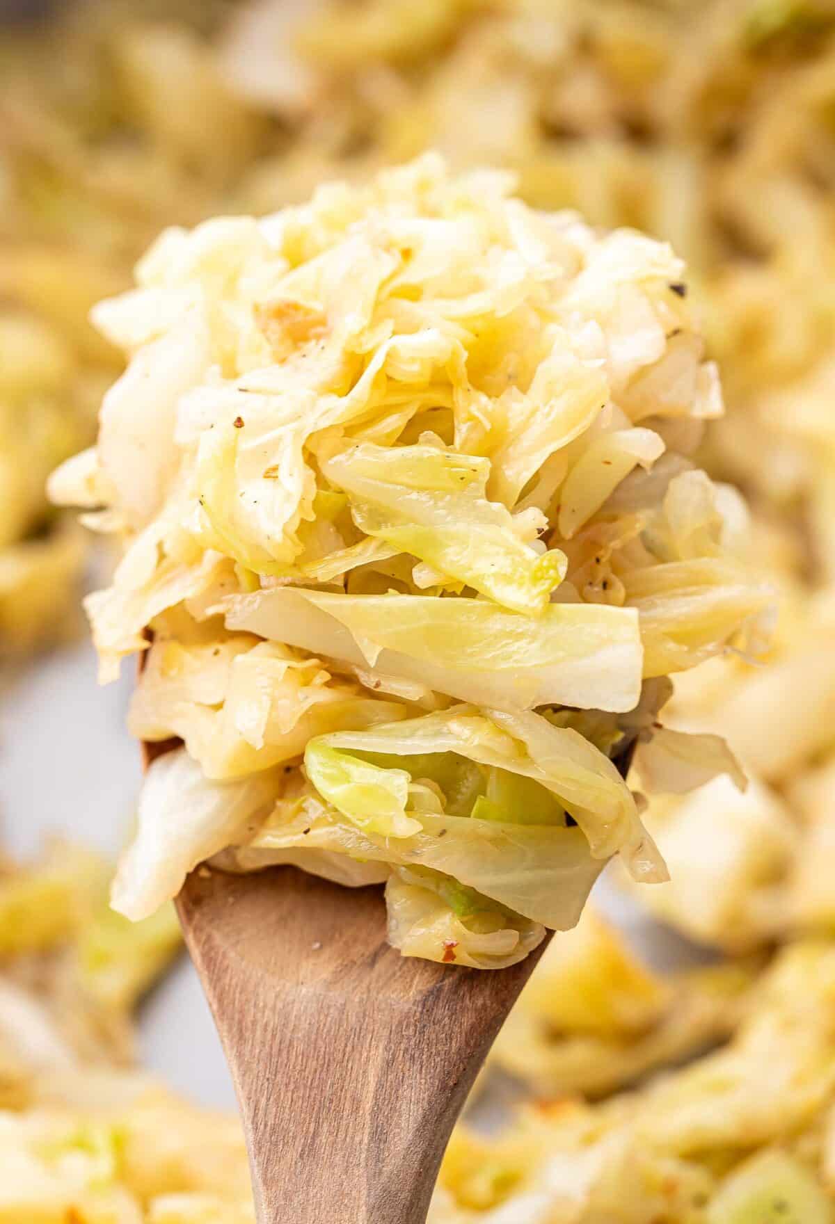 Wooden serving spoon holding up a scoop of sauteed cabbage.