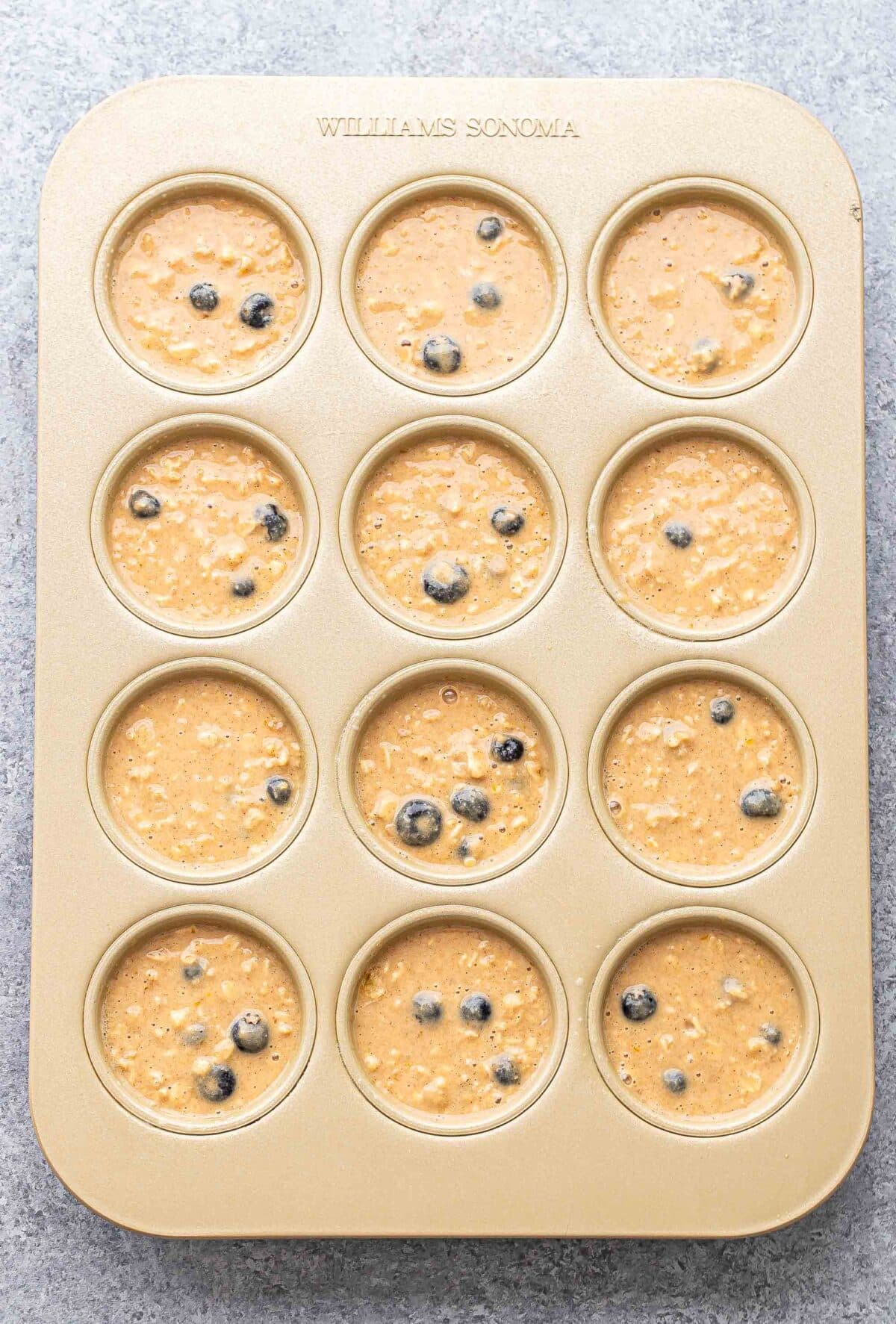 Blueberry oatmeal muffin batter in a muffin pan before it's been baked.