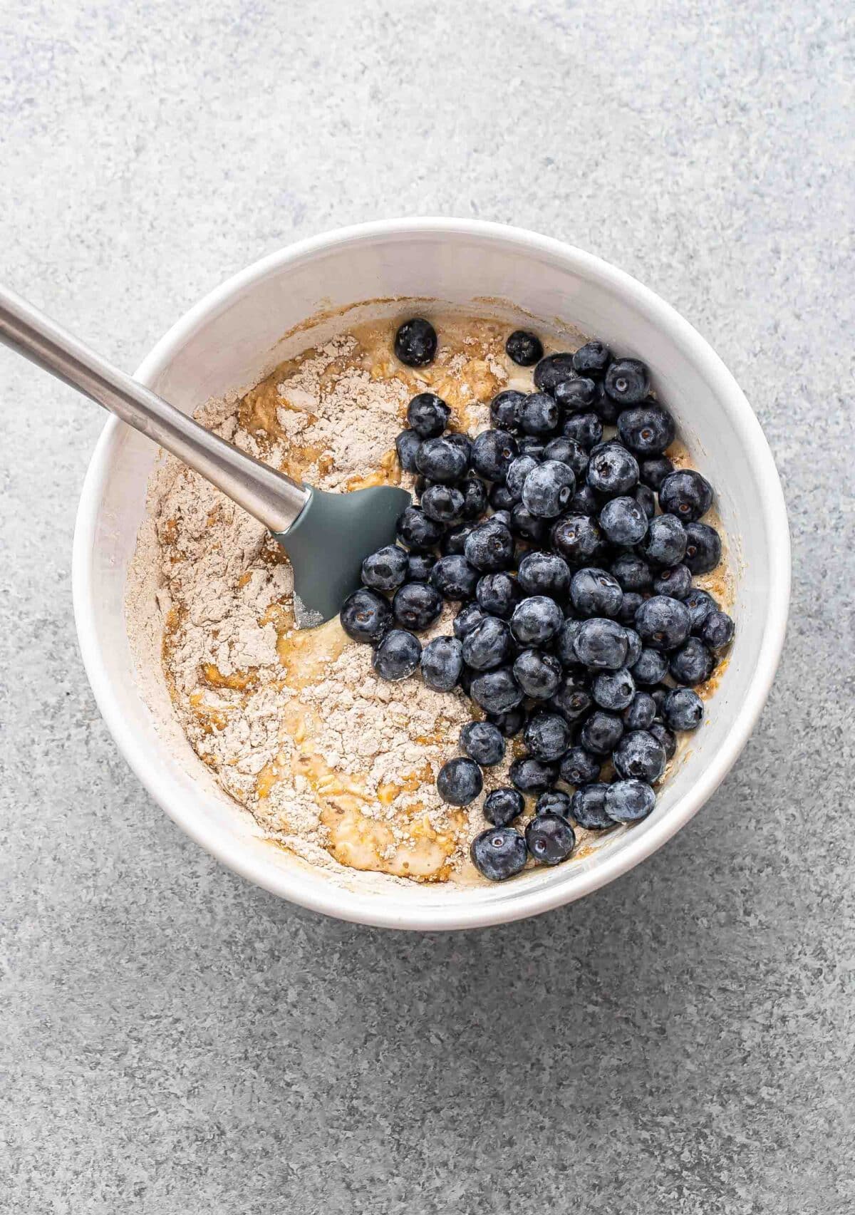 Blueberry oatmeal muffin batter in a white bowl with blueberries on top before they've been mixed in.