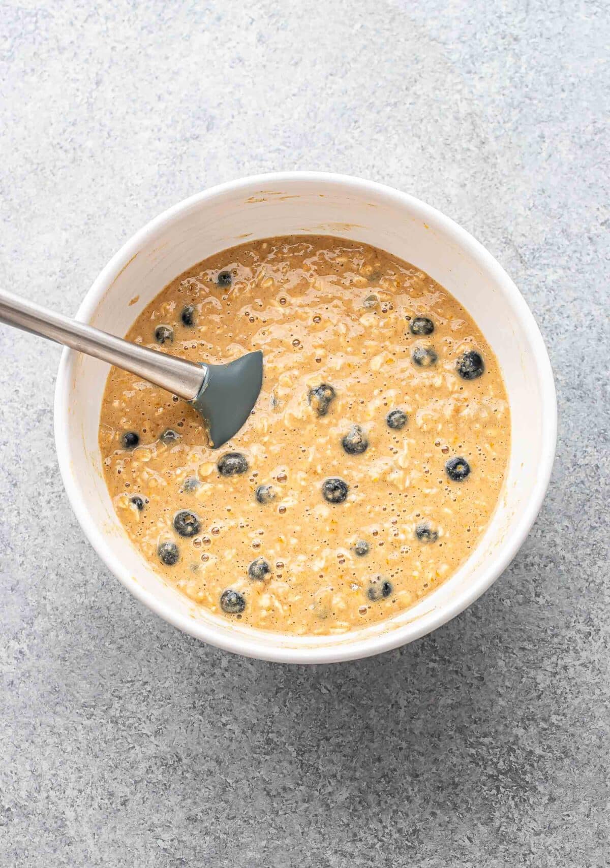 Blueberry oatmeal muffin batter in a white mixing bowl with a spatula.