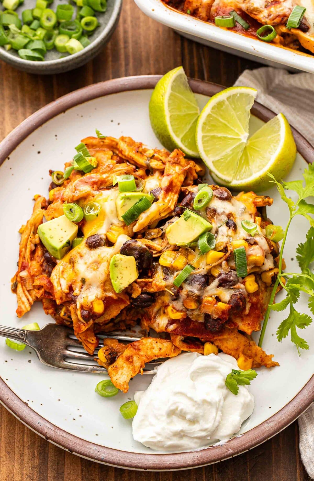 Chicken enchilada casserole on a white plate with lime wedges and sour cream.