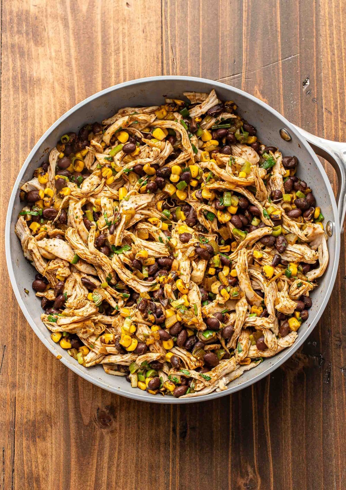 Black beans, corn, green onions, and chicken in a skillet.