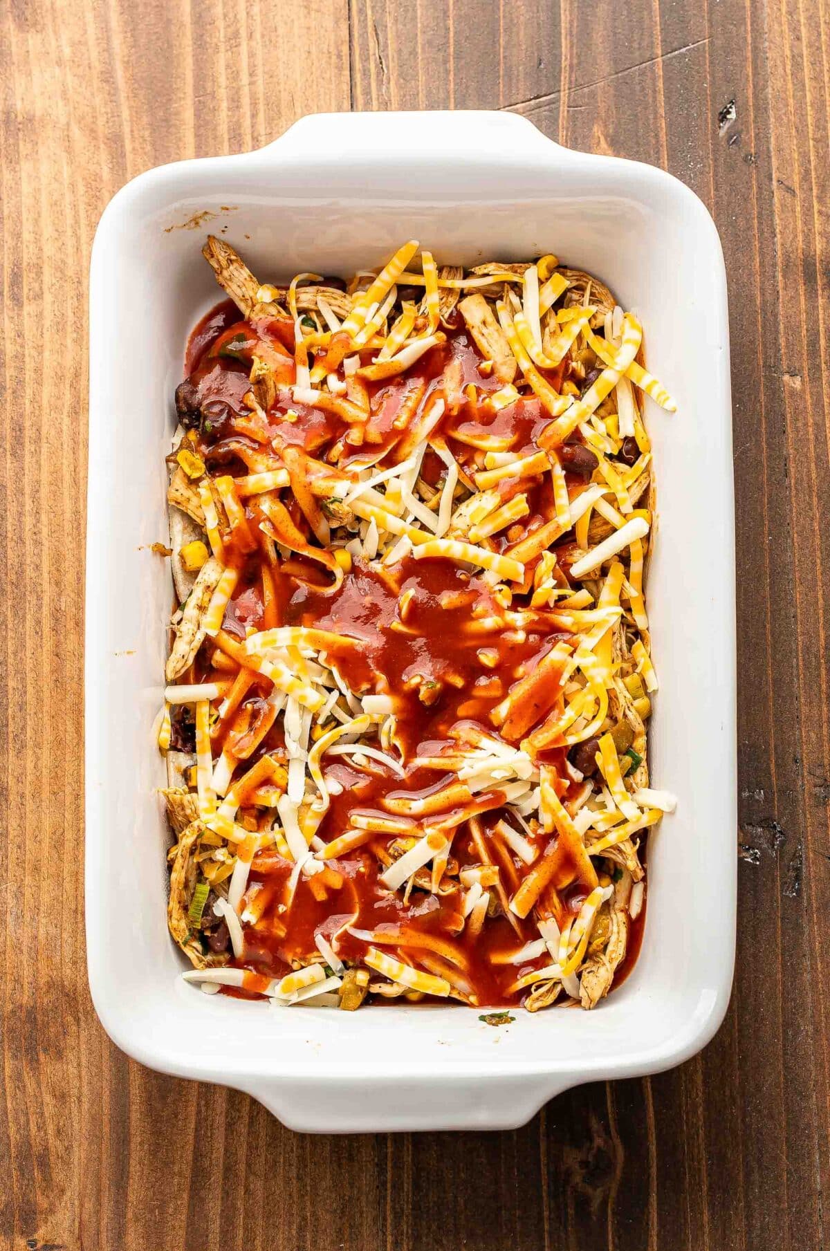 First layer of chicken enchilada casserole in a white rectangular casserole dish.