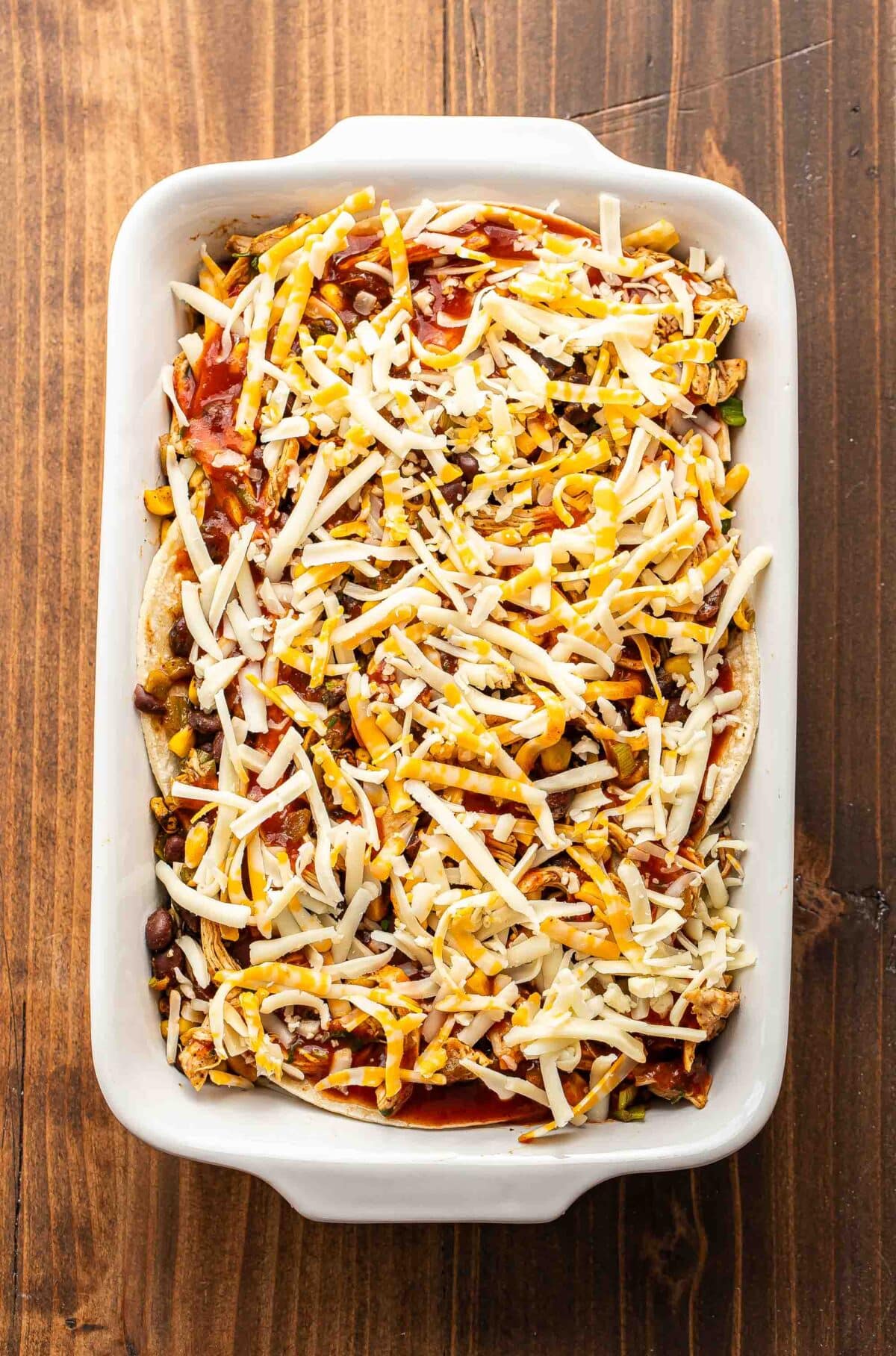 Chicken enchilada casserole in a white dish before being baked.