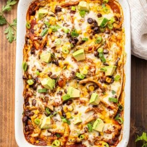 Chicken enchilada casserole garnished with avocado, green onions, and cilantro in a rectangular white dish.