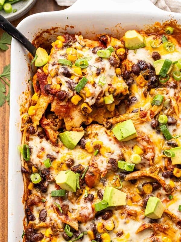 Black serving spoon scooping up chicken enchilada casserole out of the white baking dish.