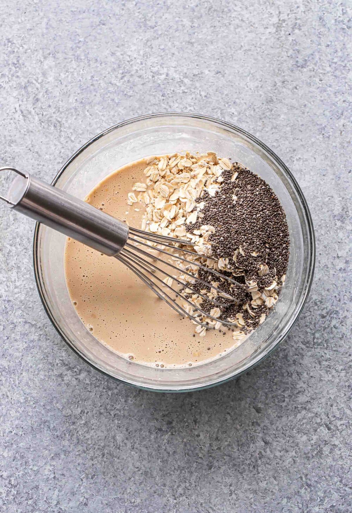 Wet ingredients for coffee overnight oats in a mixing bowl with a whisk. Oats and chia seeds are on top and haven't been mixed in.