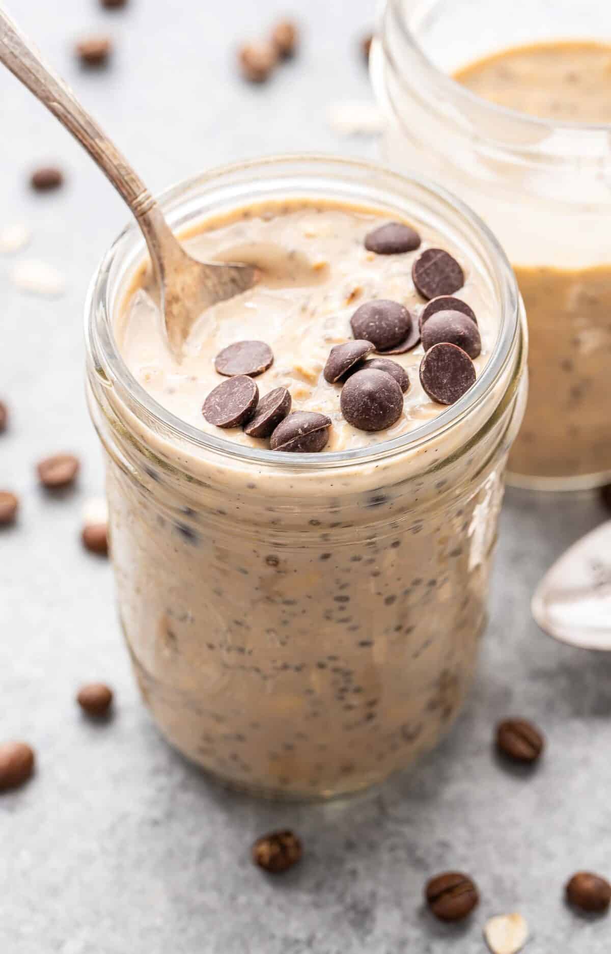 Coffee overnight oats in a glass jar with a spoon with chocolate chips on top.