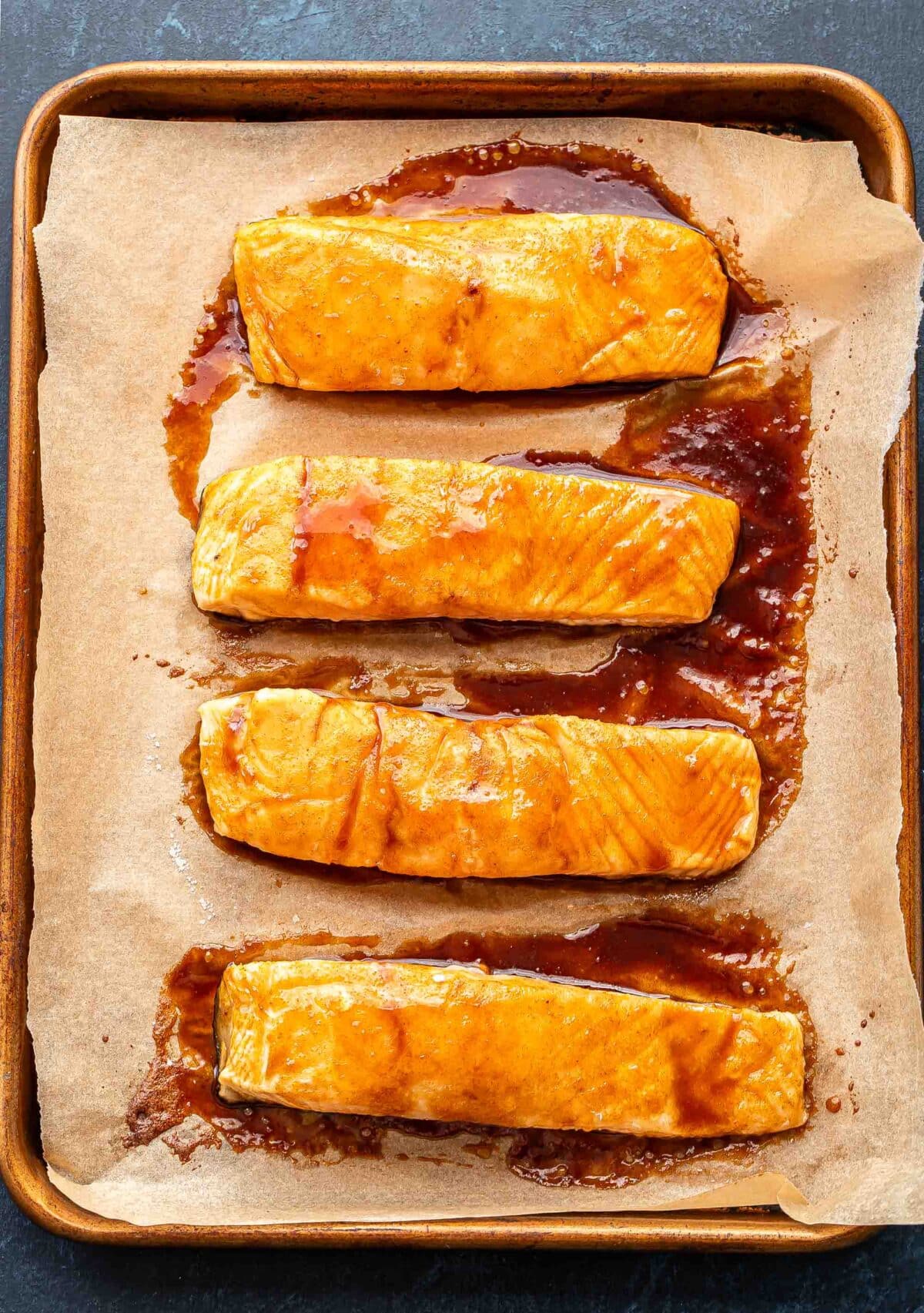 Four baked maple glazed salmon fillets on a parchment paper lined sheet pan.