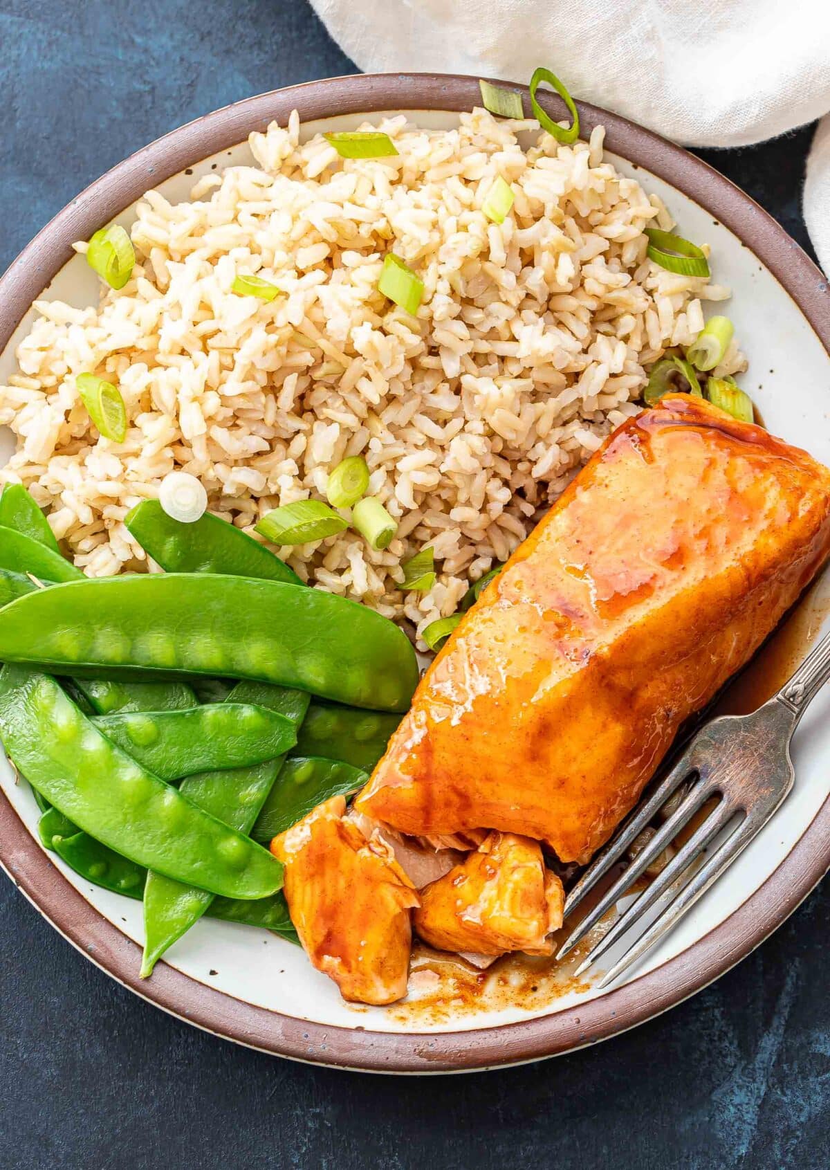 Maple glazed salmon fillet on a plate with snow peas and rice.