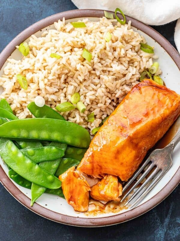 Maple glazed salmon fillet on a plate with snow peas and rice.