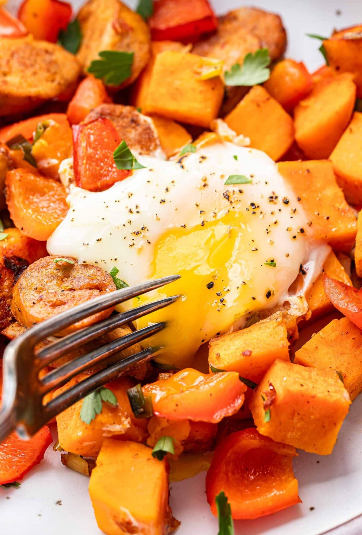 Fork cutting into egg yolk on top of sweet potato hash.