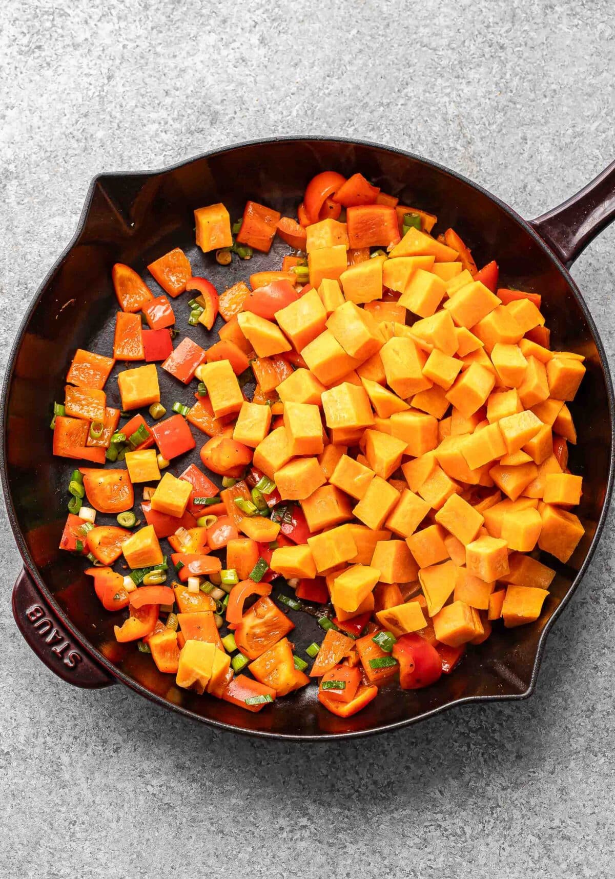 Red bell peppers, sweet potato cubes, and green onion in a skillet.