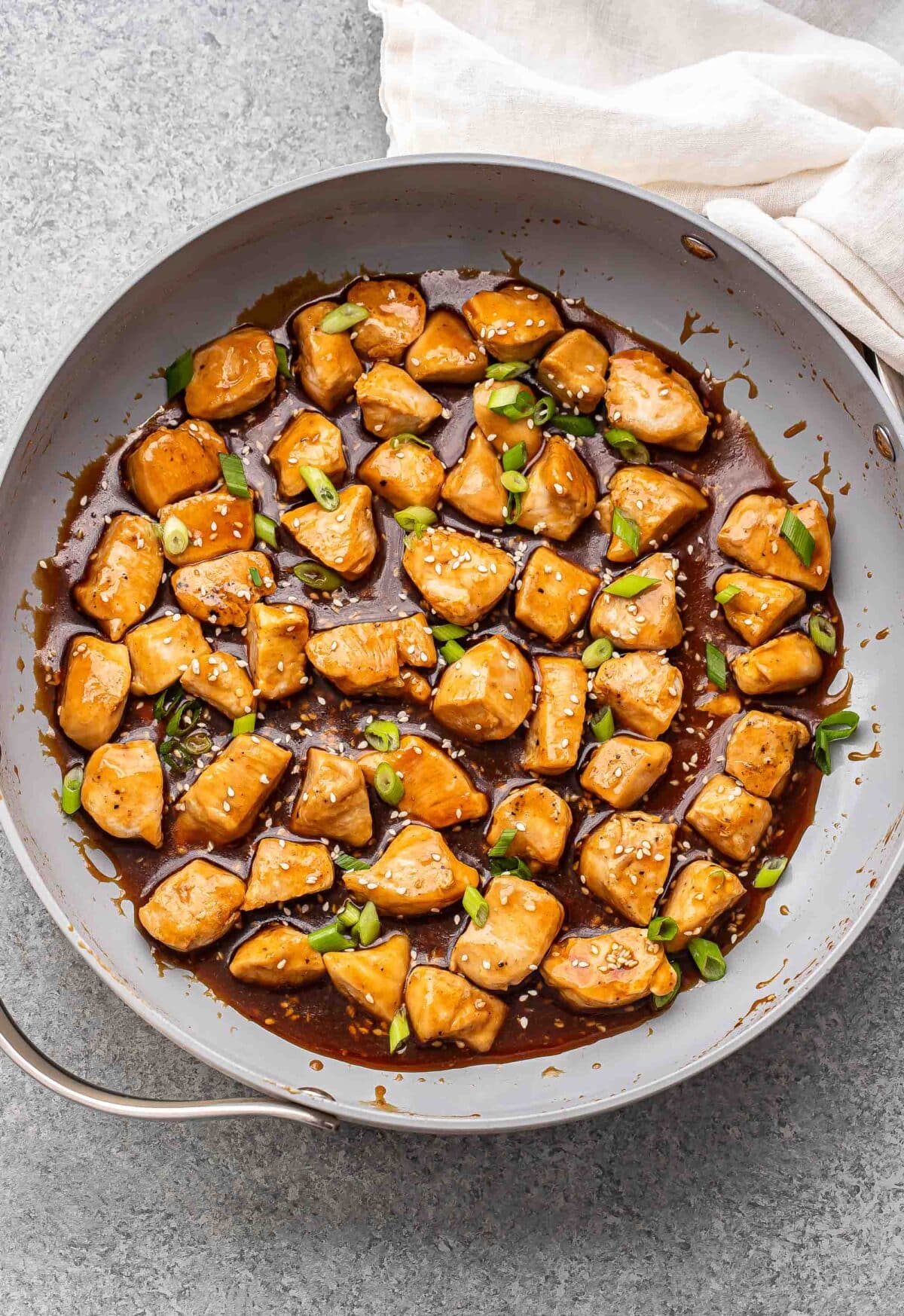 Teriyaki chicken in a skillet. The chicken is garnished with sesame seeds and green onions.