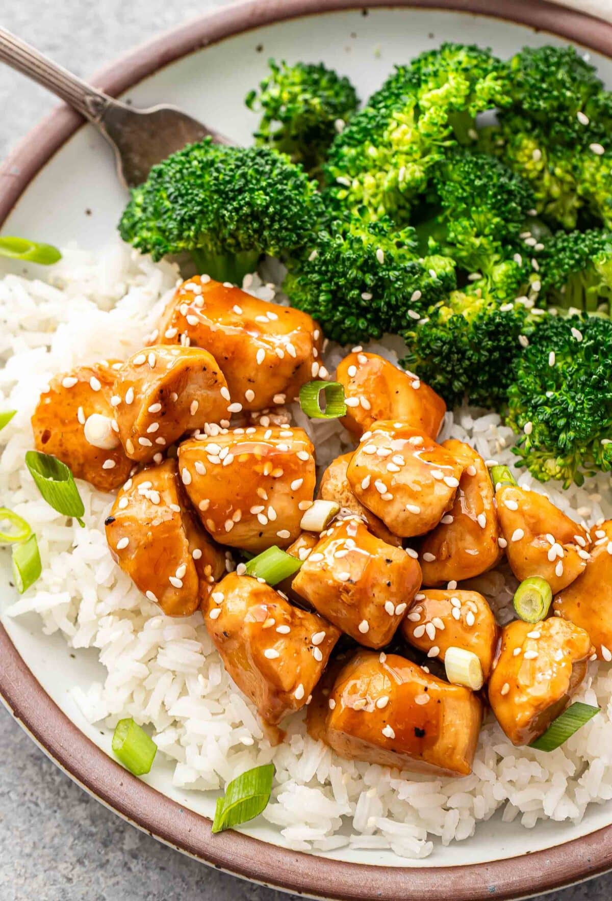Teriyaki chicken on top of rice with steamed broccoli on the side.