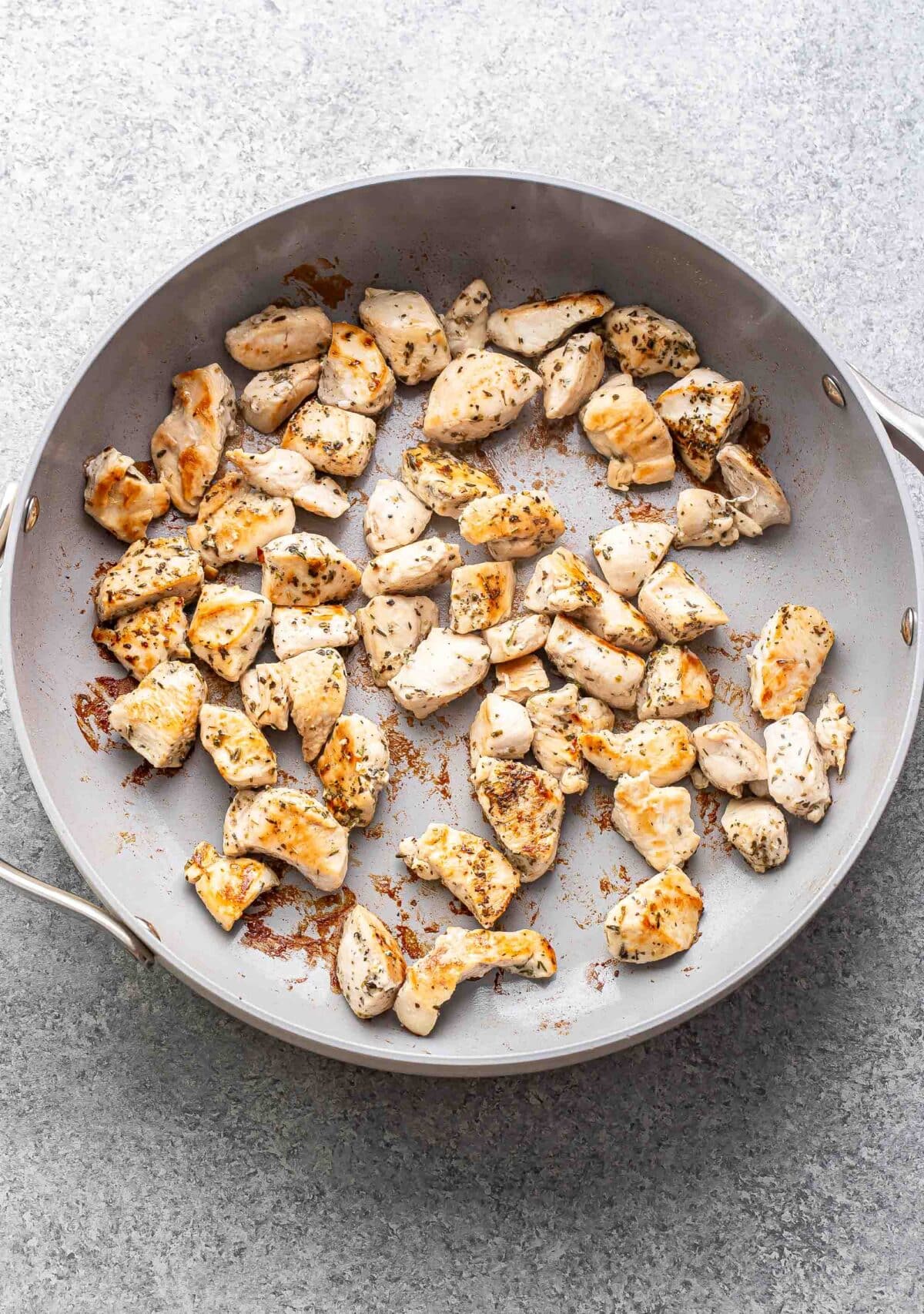 Pieces of cooked chicken in a skillet.