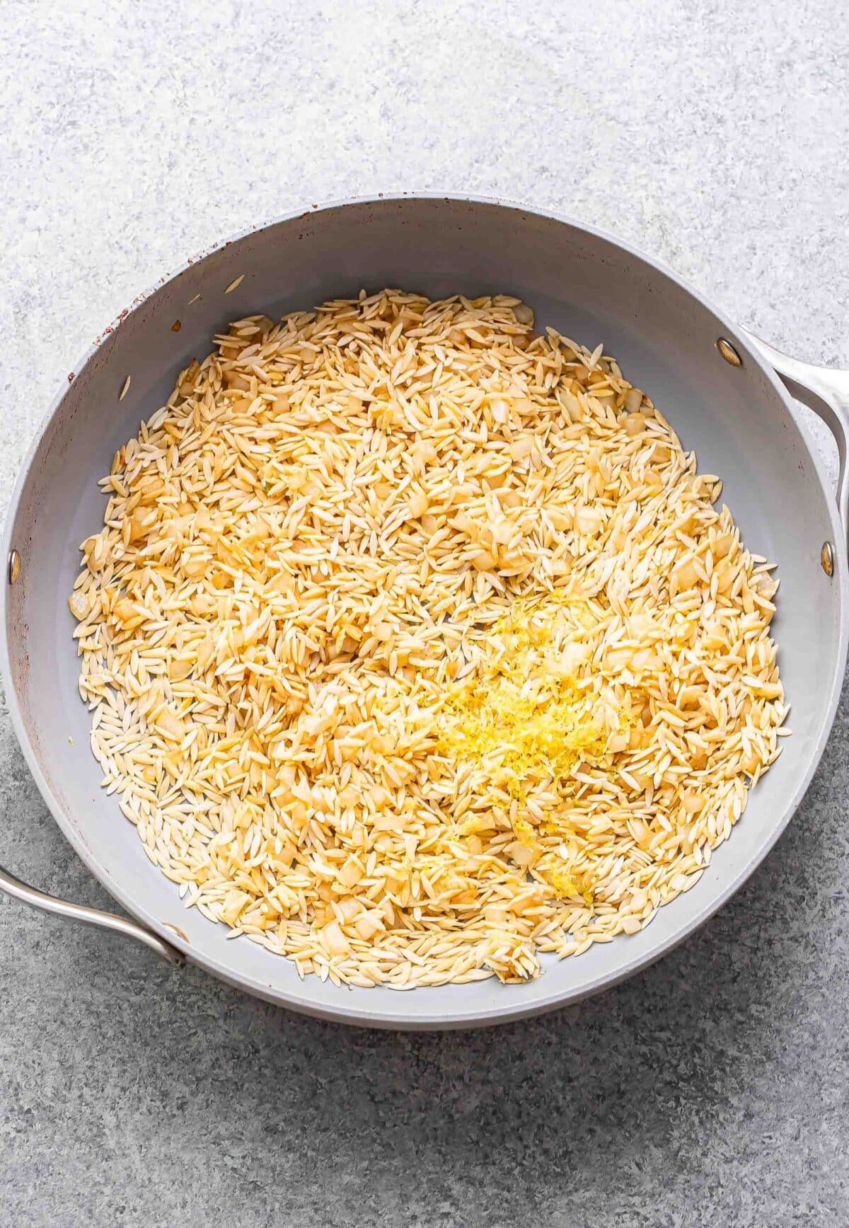 Orzo, onion, garlic and lemon zest in a skillet before it's been cooked.