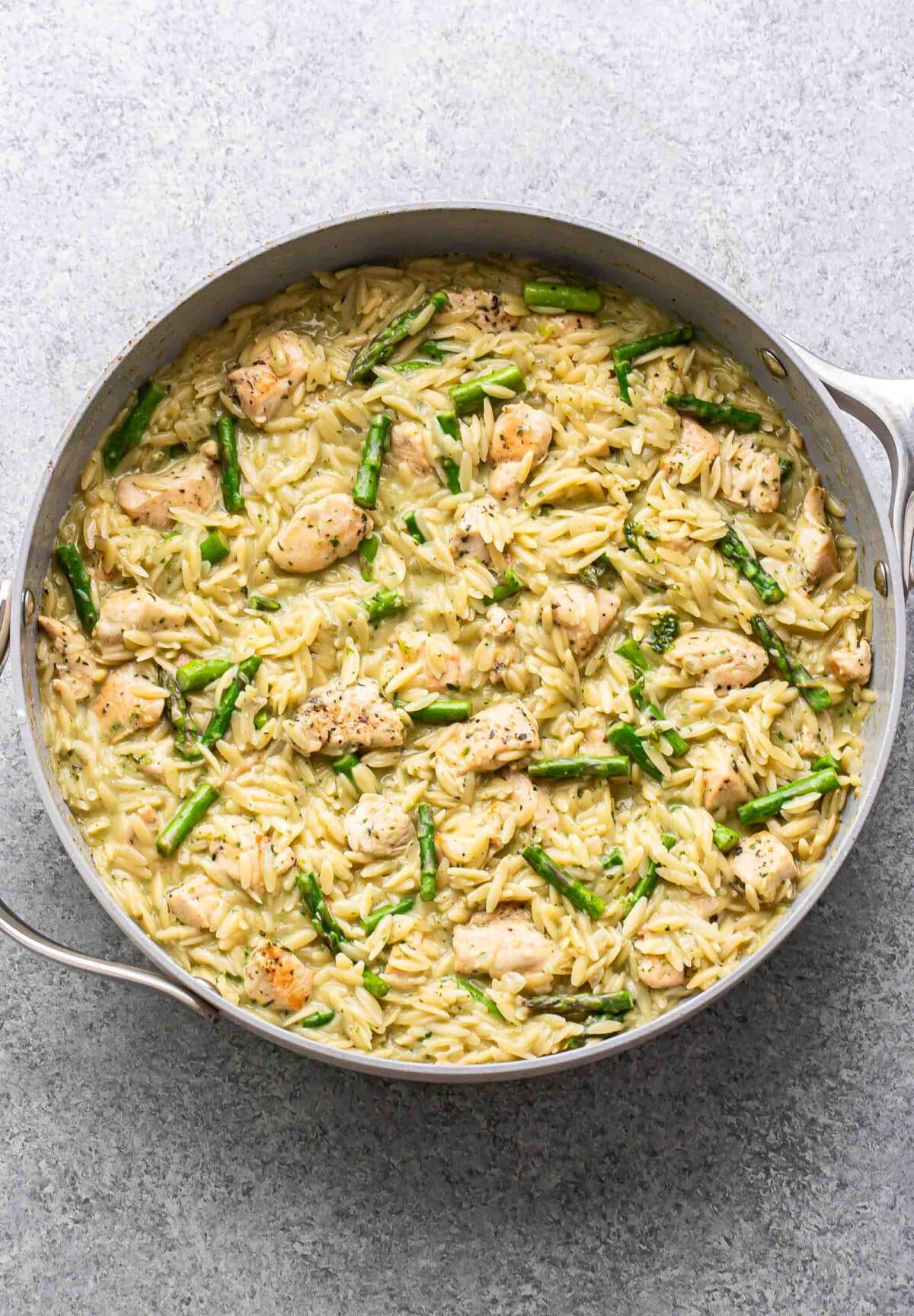 Creamy orzo with chicken, asparagus, and pesto in a skillet.