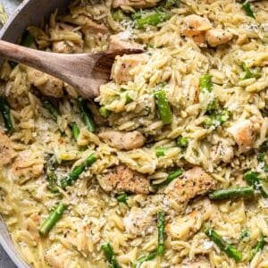 cream asparagus orzo with chicken and pesto in a pan with a wooden serving spoon.