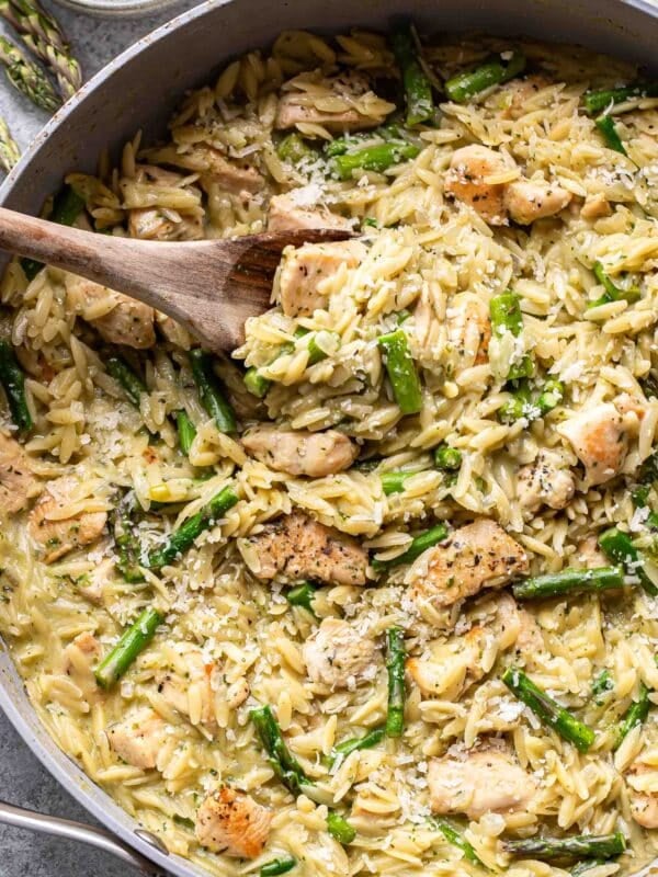 cream asparagus orzo with chicken and pesto in a pan with a wooden serving spoon.