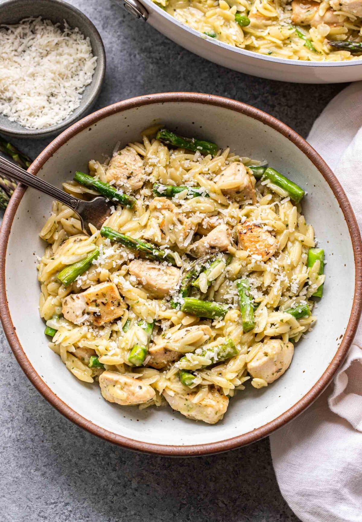 Asparagus chicken orzo in a white bowl with a fork.