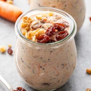 A jar of carrot cake overnight oats topped with raisins and chopped walnuts.
