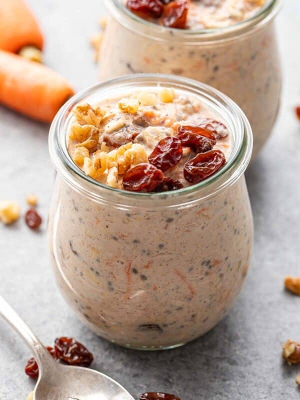 A jar of carrot cake overnight oats topped with raisins and chopped walnuts.