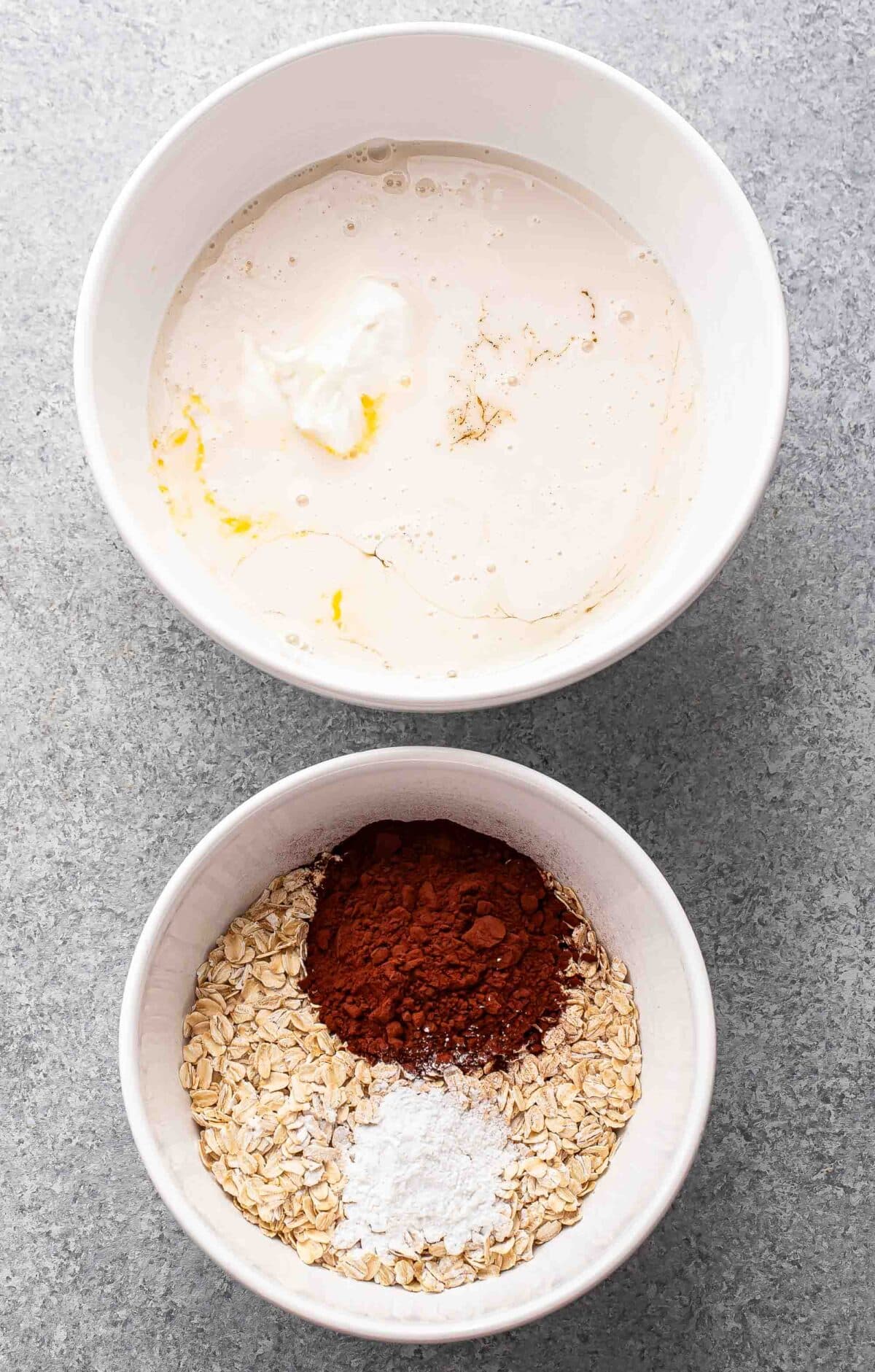 Wet ingredients for chocolate baked oatmeal in a large white mixing bowl and dry ingredients in a small white mixing bowl.