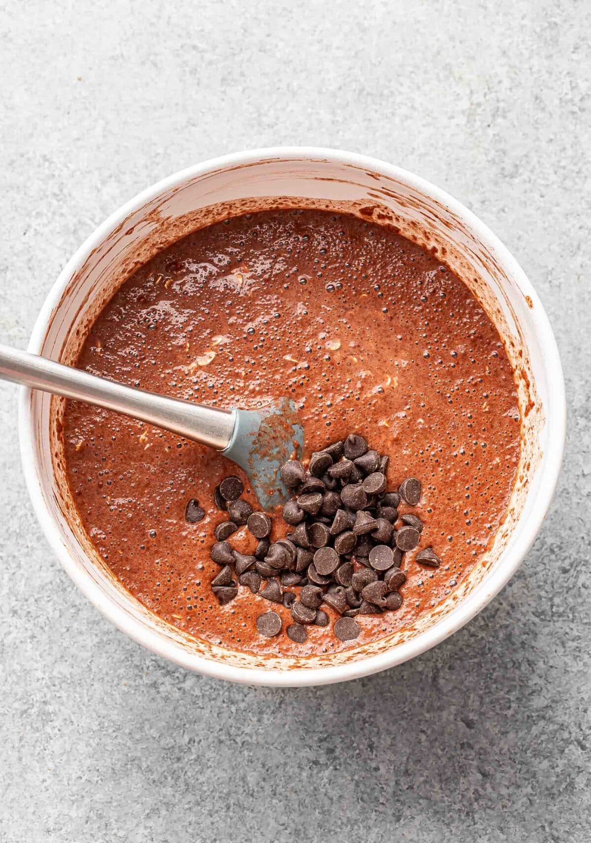 Chocolate baked oatmeal mixture with chocolate chips in a white mixing bowl before it's been baked.