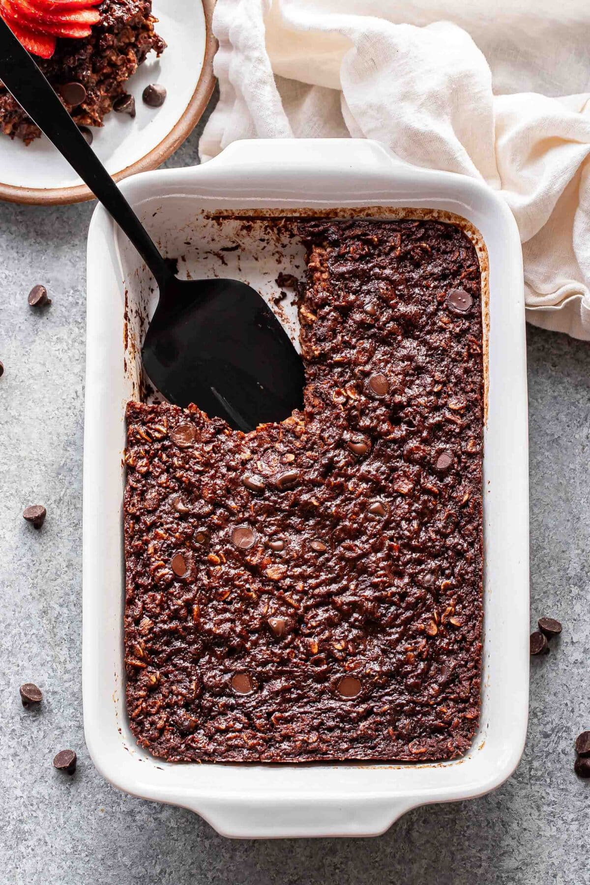 Chocolate baked oats in a white baking dish with a piece cut out and a black serving spoon in the dish.