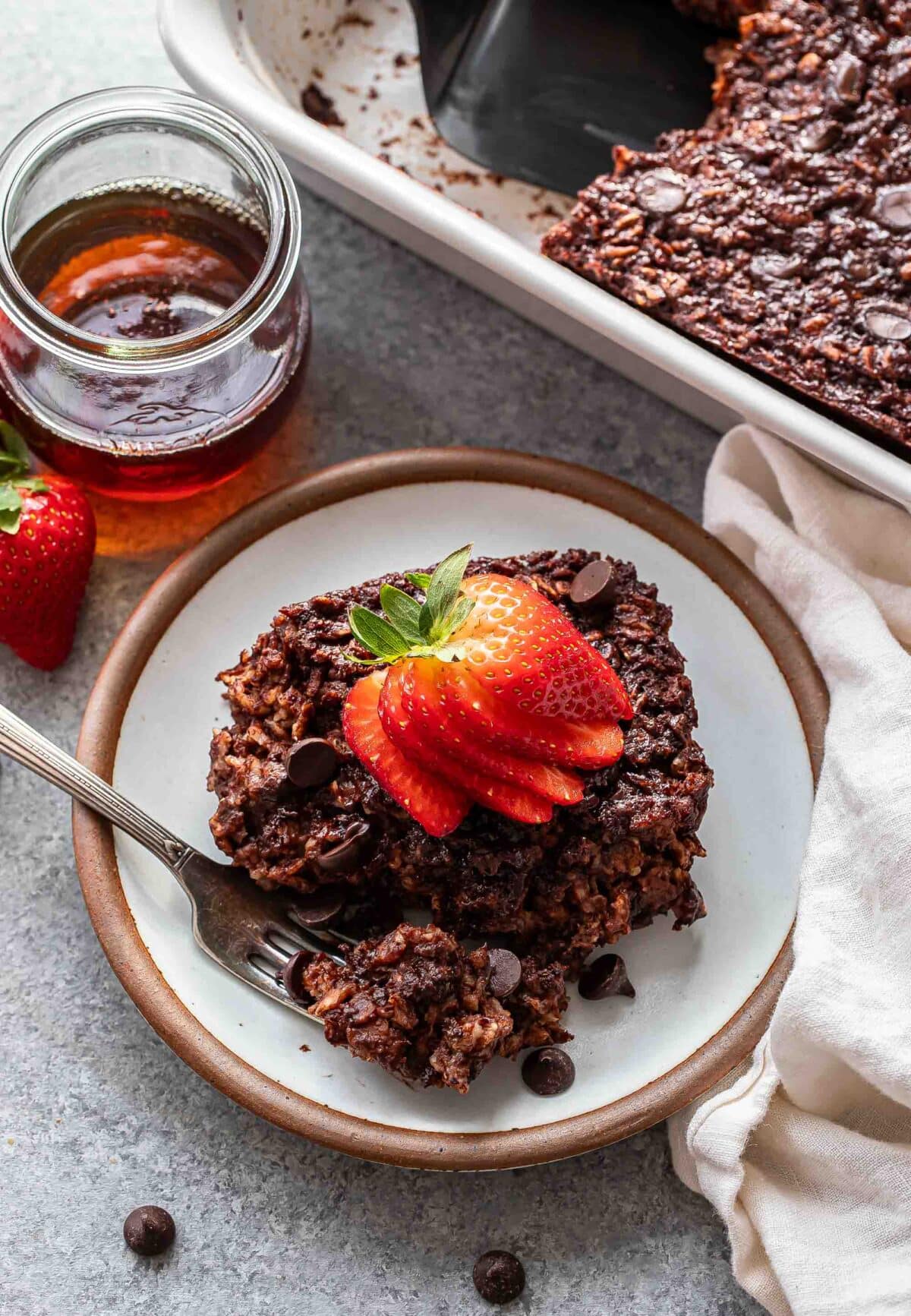 A piece of chocolate baked oatmeal topped with sliced strawberries on a white plate with a fork.