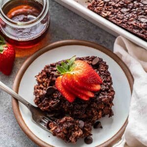 A piece of chocolate baked oatmeal topped with sliced strawberries on a white plate with a fork.