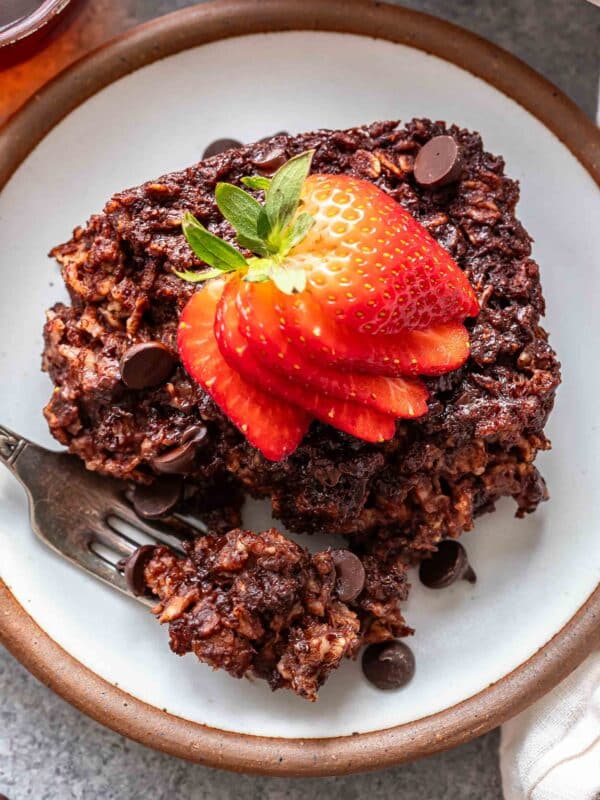 A piece of chocolate baked oatmeal topped with sliced strawberries on a white plate with a fork.