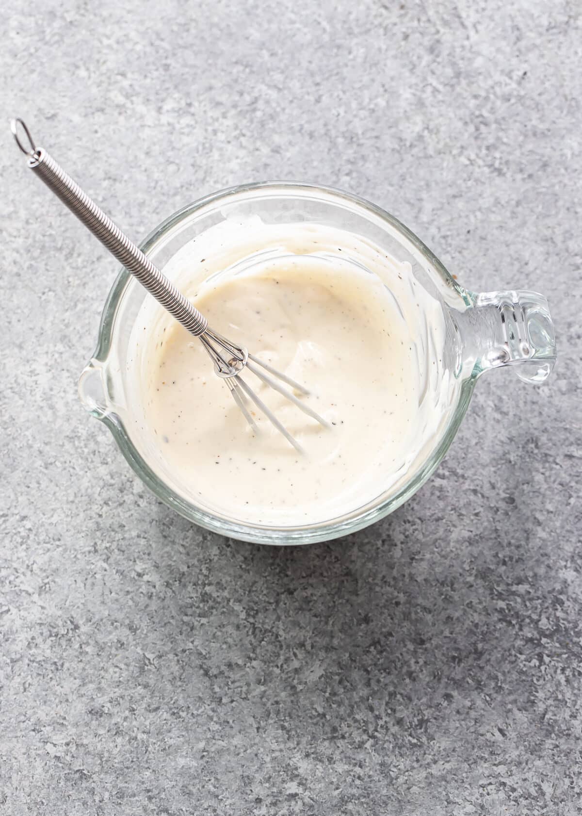 Creamy dressing for pea salad in a glass measuring cup with a whisk.