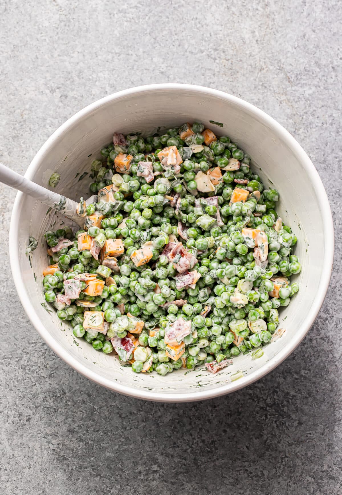 Creamy pea salad in a white mixing bowl with a spatula.