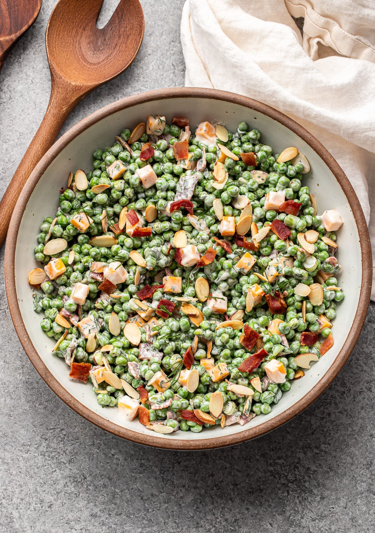 Creamy pea salad with bacon and cubes of cheddar cheese in a white serving bowl.