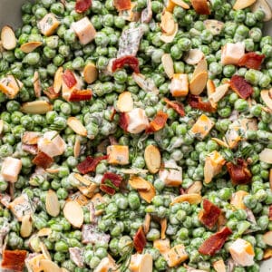 Creamy pea salad with bacon and cubes of cheddar cheese in a white serving bowl.