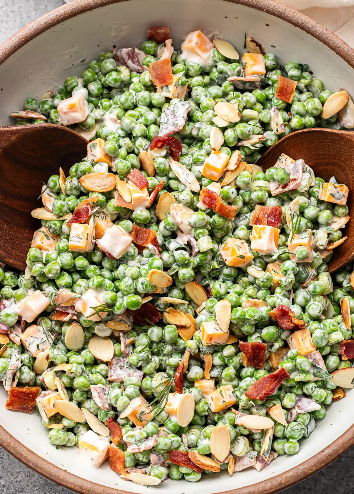 Creamy pea salad with bacon and cheese in a serving bowl with wooden serving spoons.