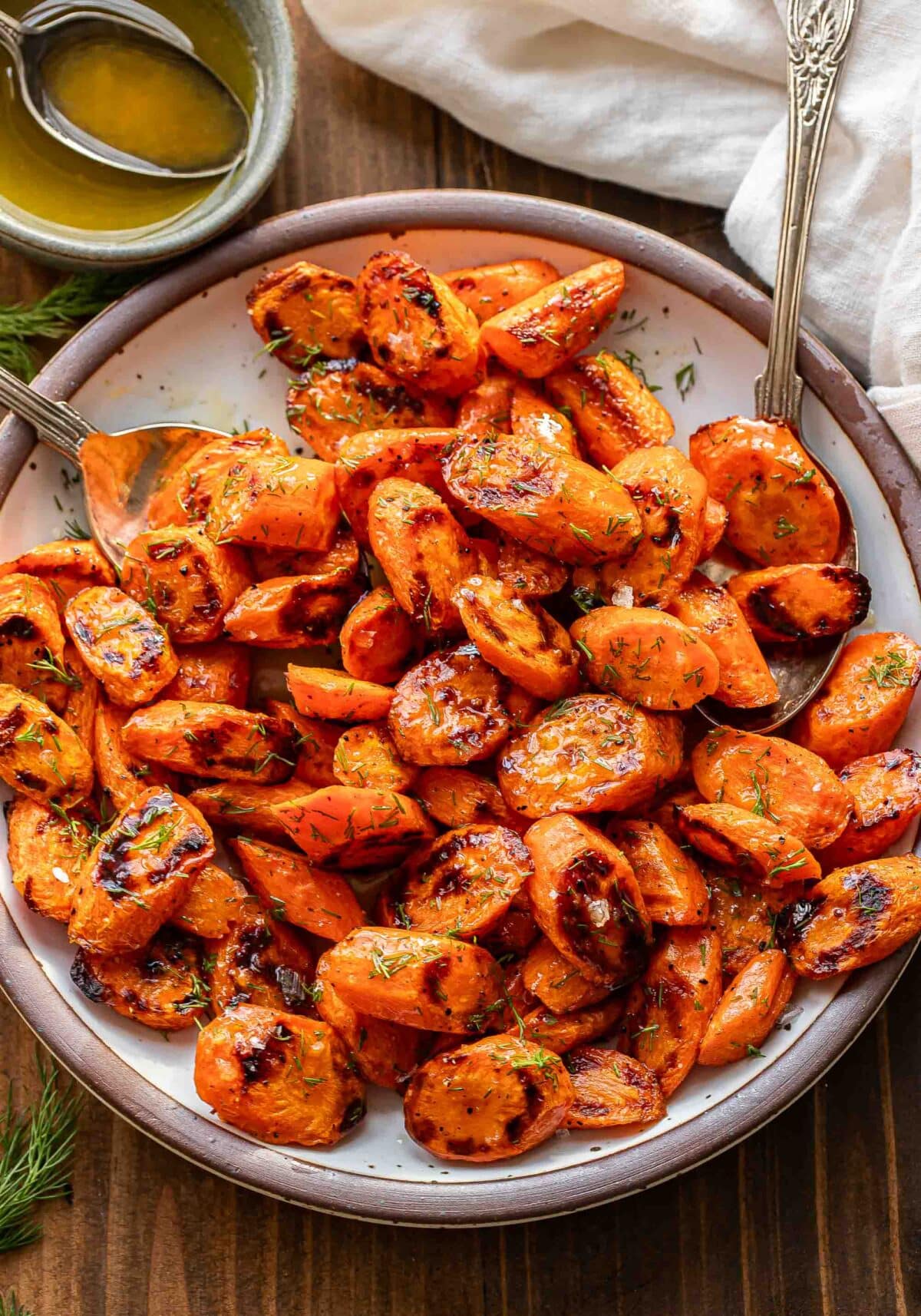 Roasted carrots with honey butter and dill on a white plate with two spoons.