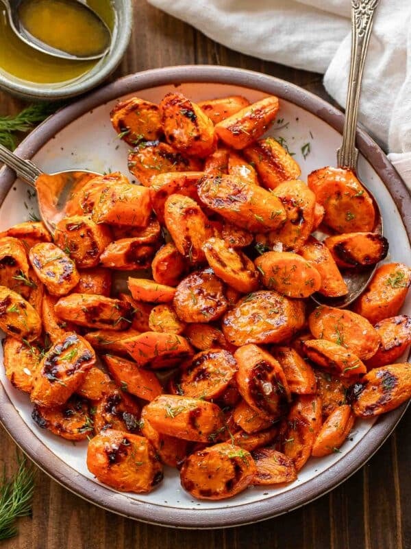Roasted carrots with honey butter and dill on a white plate with two spoons.