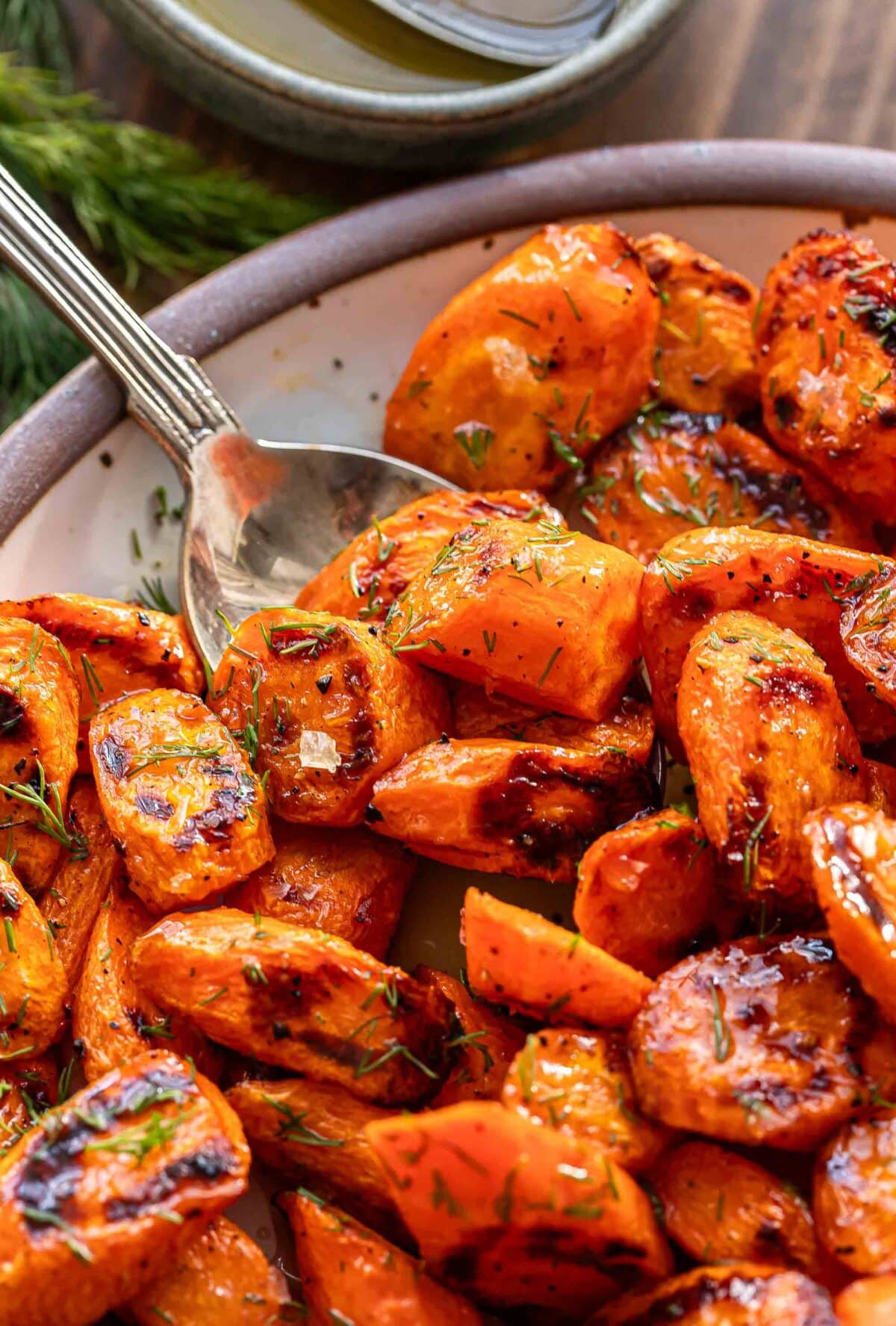 Spoon scooping up honey roasted carrots off of a white plate.