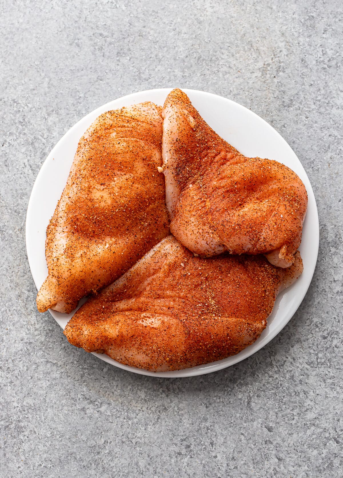 Seasoned uncooked chicken breasts on a plate.