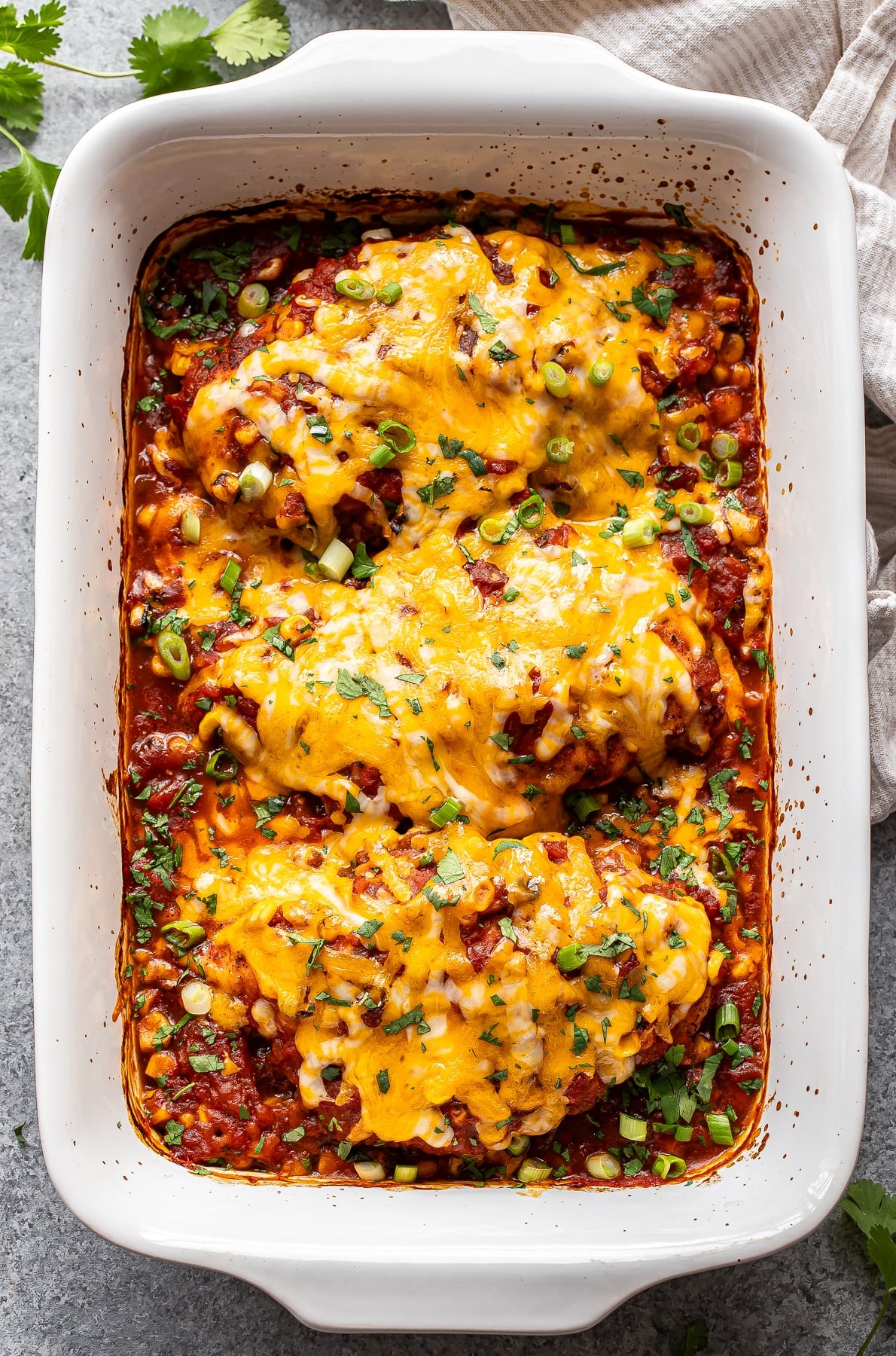 Baked salsa chicken topped with melted cheese, green onions, and cilantro in a white casserole dish.