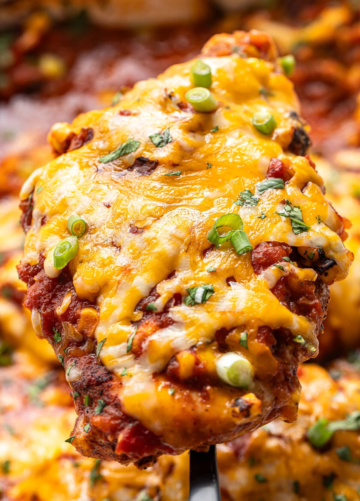 Serving spoon holding up a chicken breast topped with salsa and melted cheese.