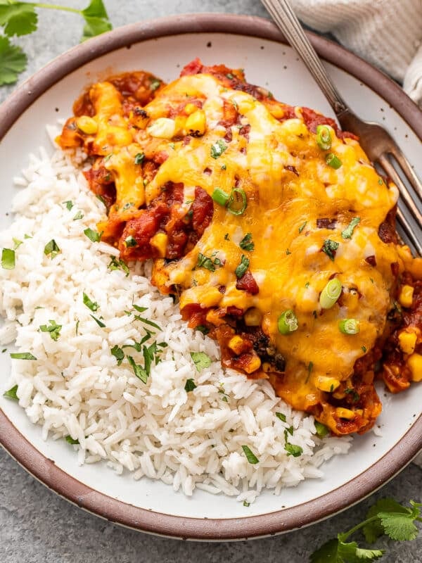 Baked salsa chicken breast with cheese on a white plate with rice.